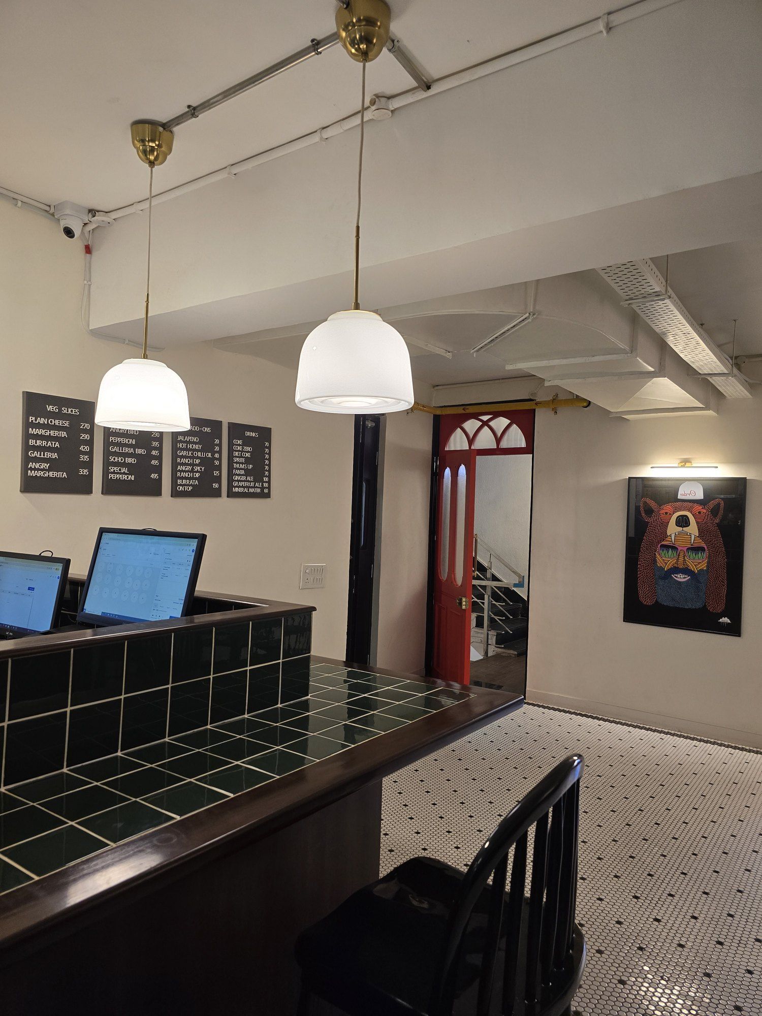 Order counter at Galaxy Slice Shop with a green tiled top, white pendant lights, menu boards and a red door