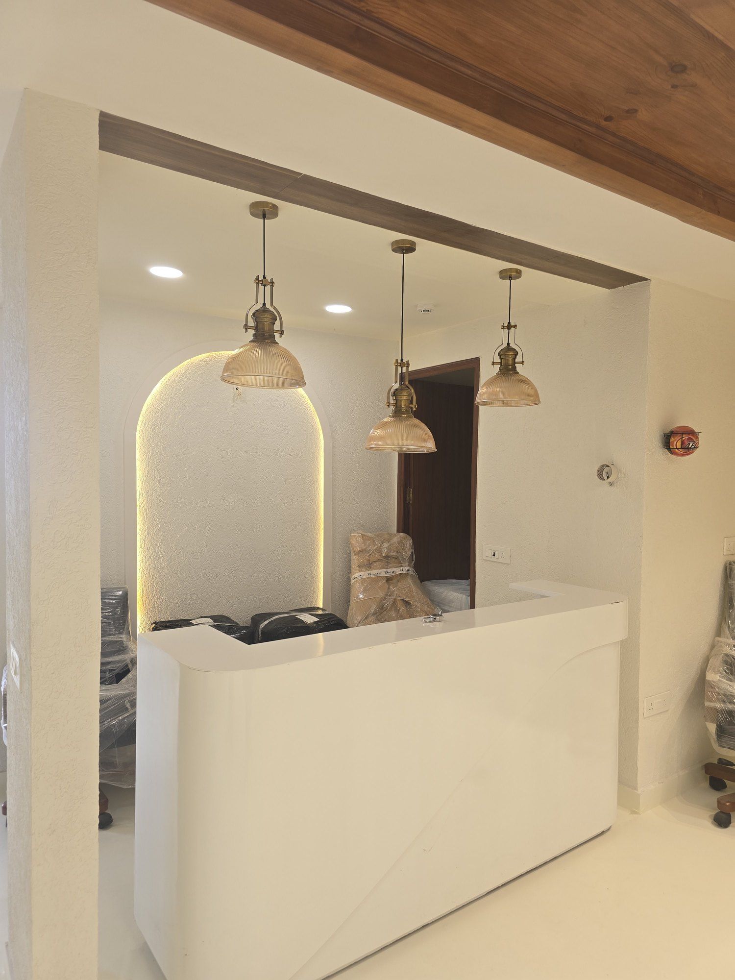 Reception at Crystal IVF with a white counter under a backlit arch, brass pendant lights and a dark timber ceiling