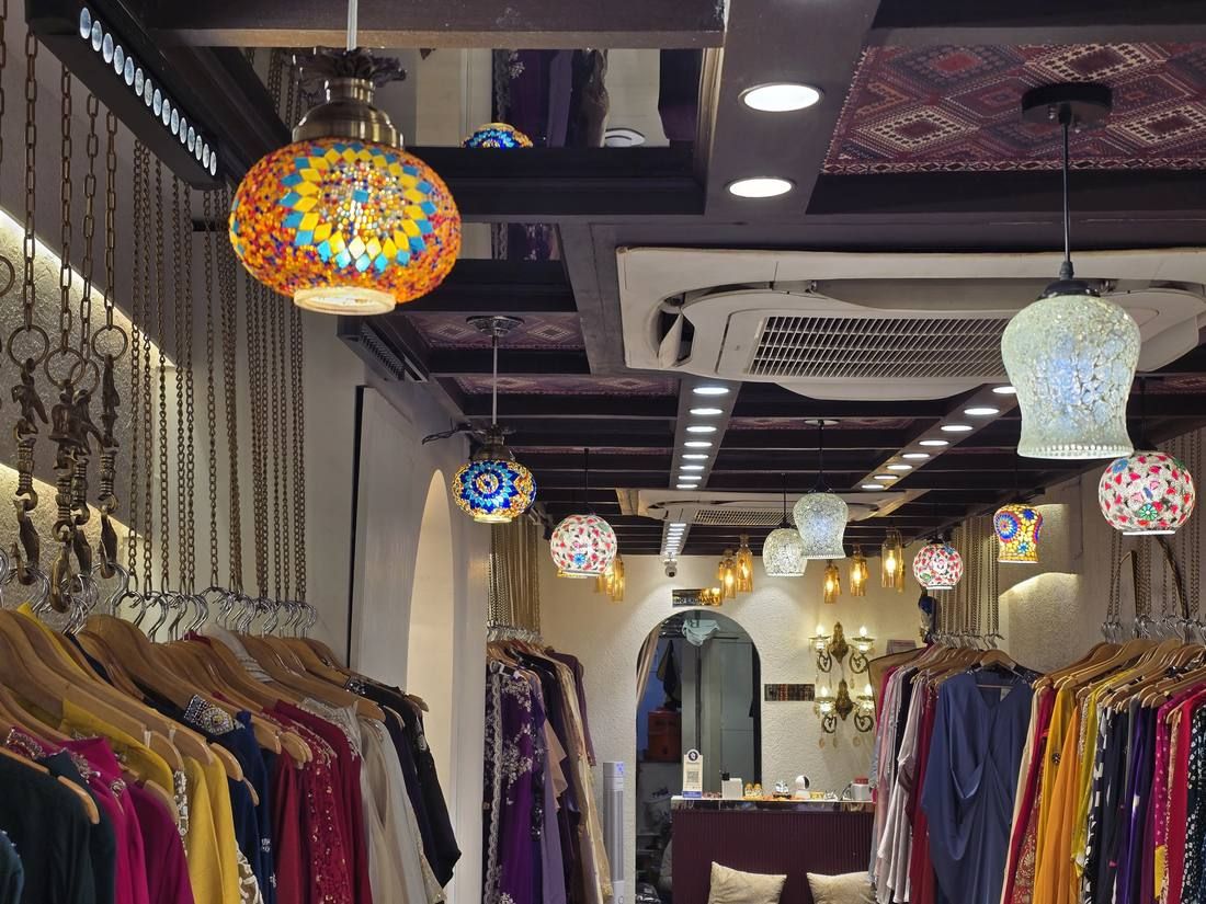 Turkish mosaic lamps hanging from a printed ceiling above racks of festive ethnic wear