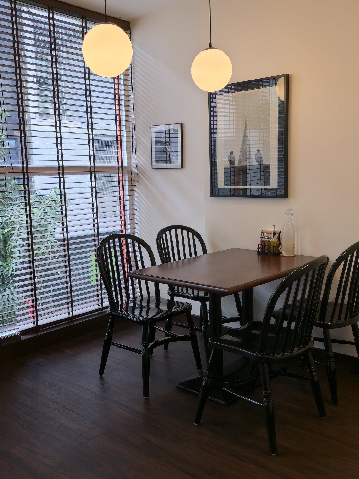Table by the window with blinds, globe pendants and framed prints