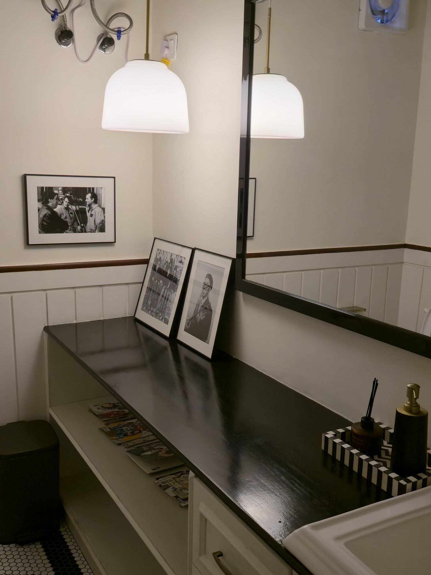 Washroom with a black counter, white panelling and framed photographs